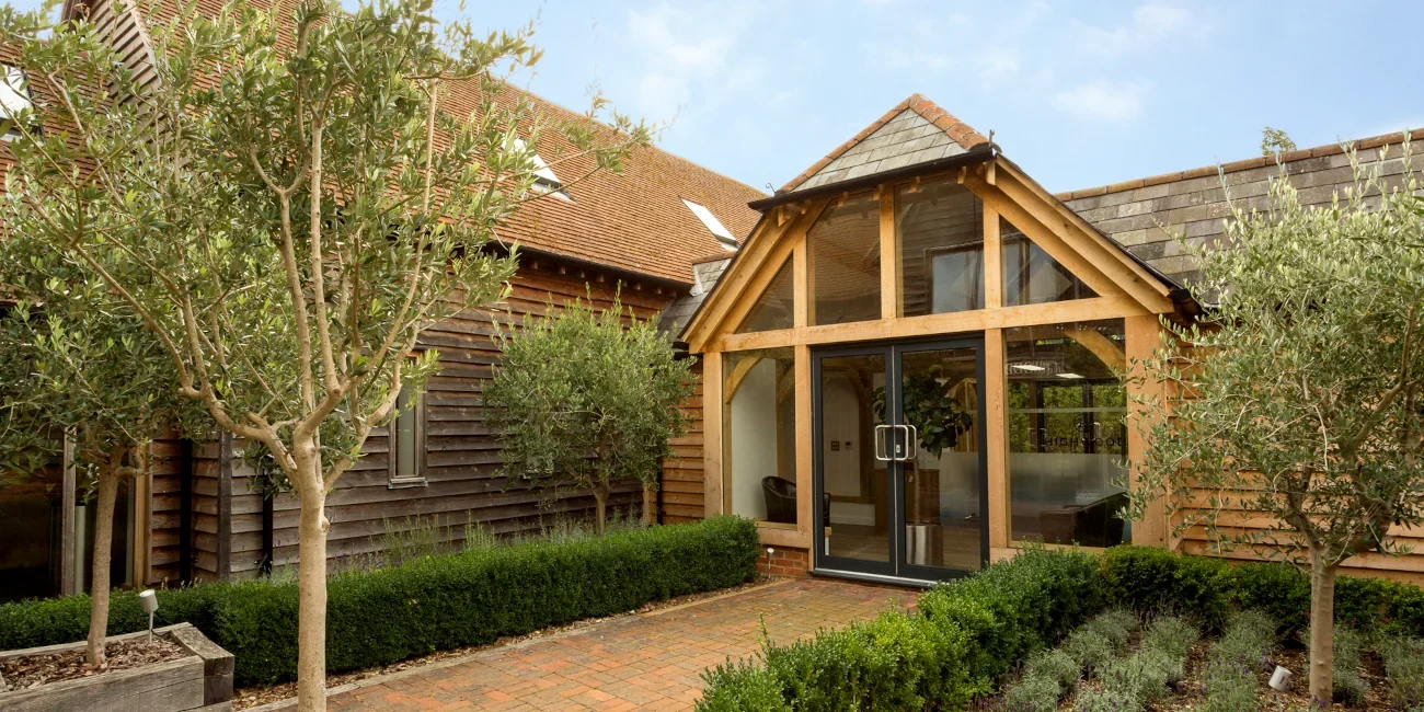 Bespoke Oak Framed Buildings In Hampshire The welcoming entrance of one of our bespoke oak framed buildings in Hampshire, featuring a vaulted glass entrance and exposed beams in the English countryside.