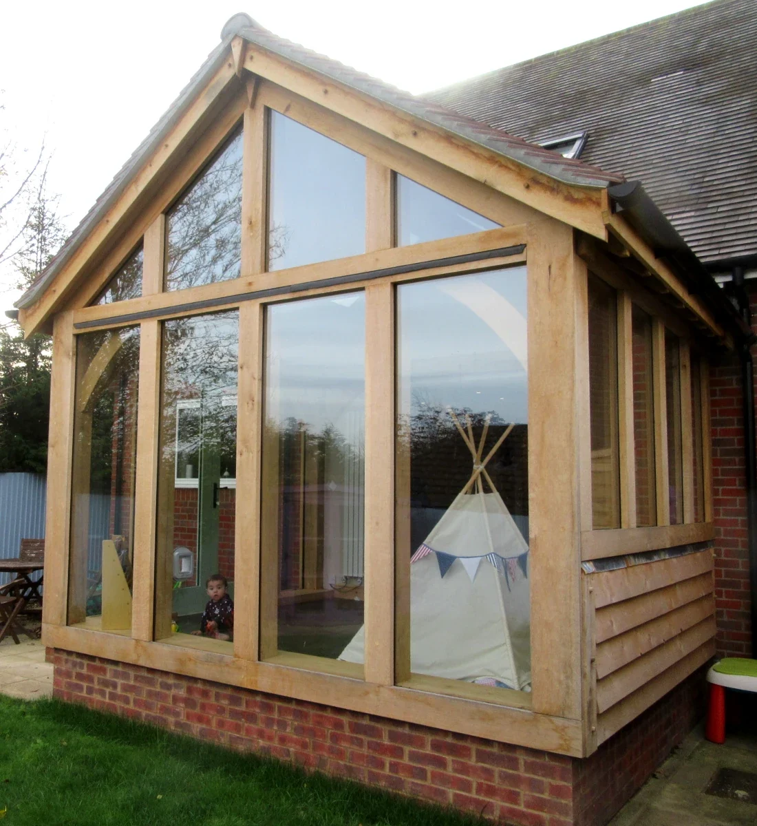 Bespoke Oak Framed Buildings In Hampshire Bespoke oak framed playroom extension in Hampshire featuring fully glazed gable end, featheredge timber cladding, clay tiled roof and brick plinth, showcasing traditional joinery techniques whilst creating a bright family space