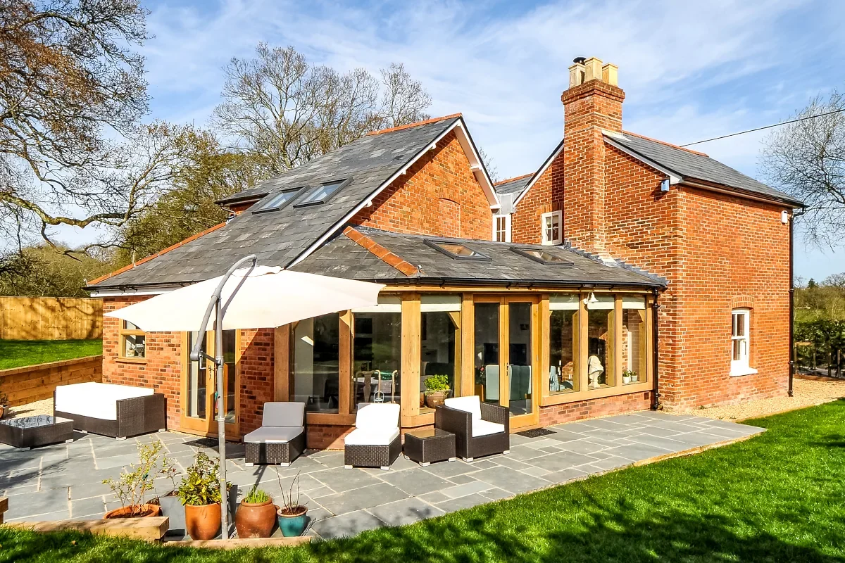 Bespoke Oak Framed Buildings In Hampshire Luxury brick home with bespoke oak framed garden room extension featuring timber posts, slate roof, and stone patio in Hampshire countryside