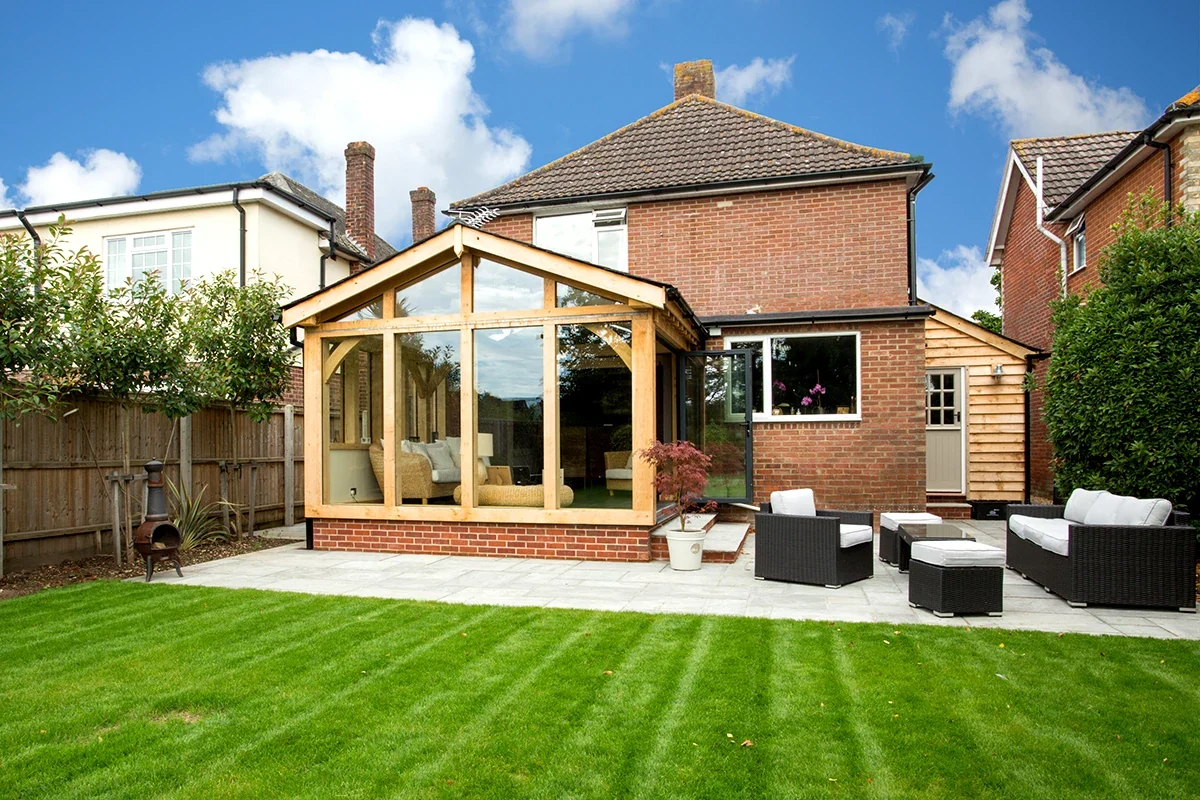 Bespoke Oak Framed Buildings In Hampshire Handcrafted bespoke oak framed garden room with full-height glazing attached to a traditional brick Hampshire home, creating a versatile extra space with beautiful garden views.