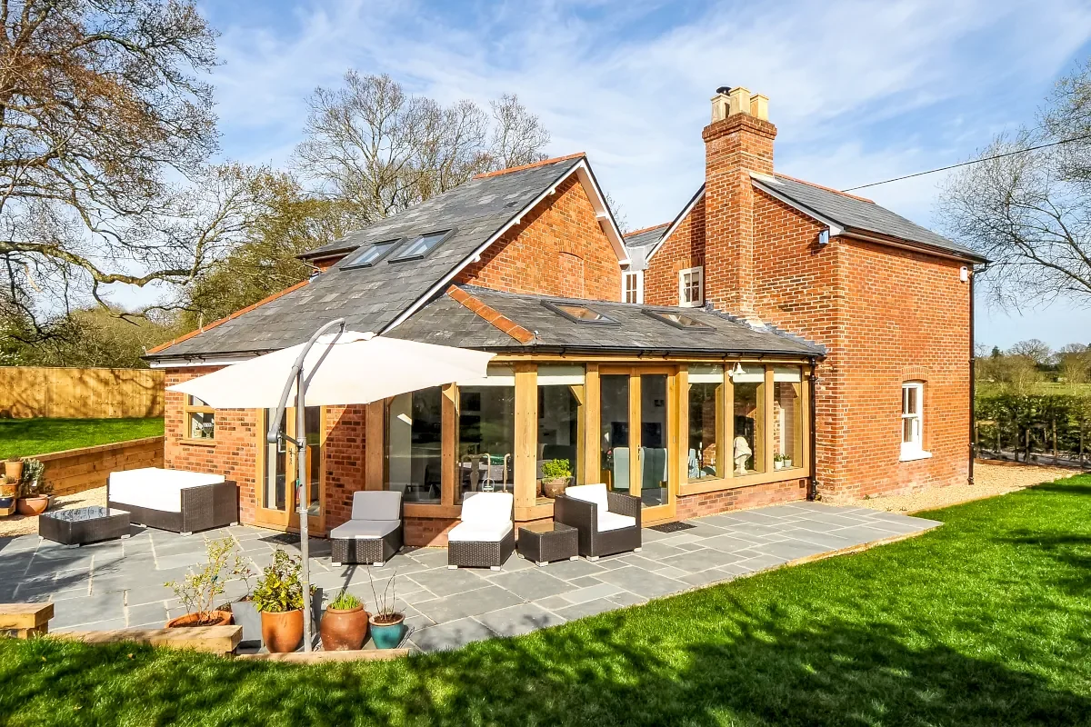 Oak Framed Extensions Hampshire Oak framed extension with full-width glass doors on Hampshire brick country house, featuring slate roof, stone patio and rural garden setting