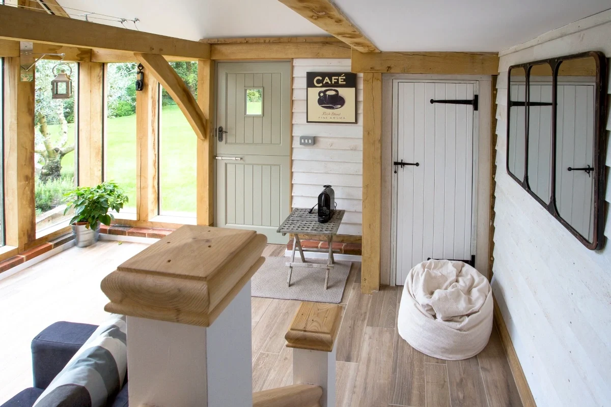 Oak Framed Extensions Hampshire Interior of oak framed garden extension in Hampshire with exposed beams, wooden flooring, practical split door and large windows overlooking garden