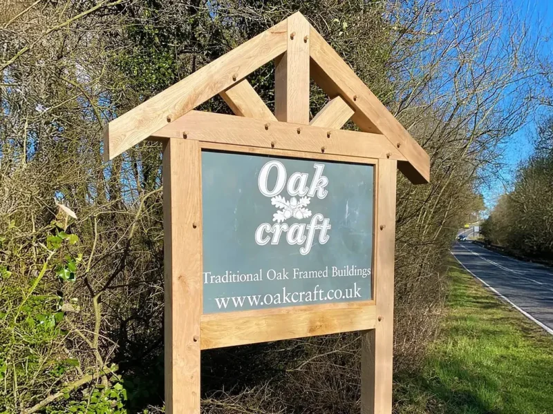 Roadside oak property sign with triangular gabled frame, traditional joinery and green signboard marking entrance to business premises