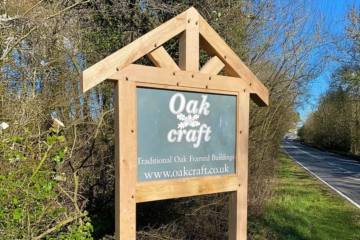 Roadside oak property sign with triangular gabled frame, traditional joinery and green signboard marking entrance to business premises