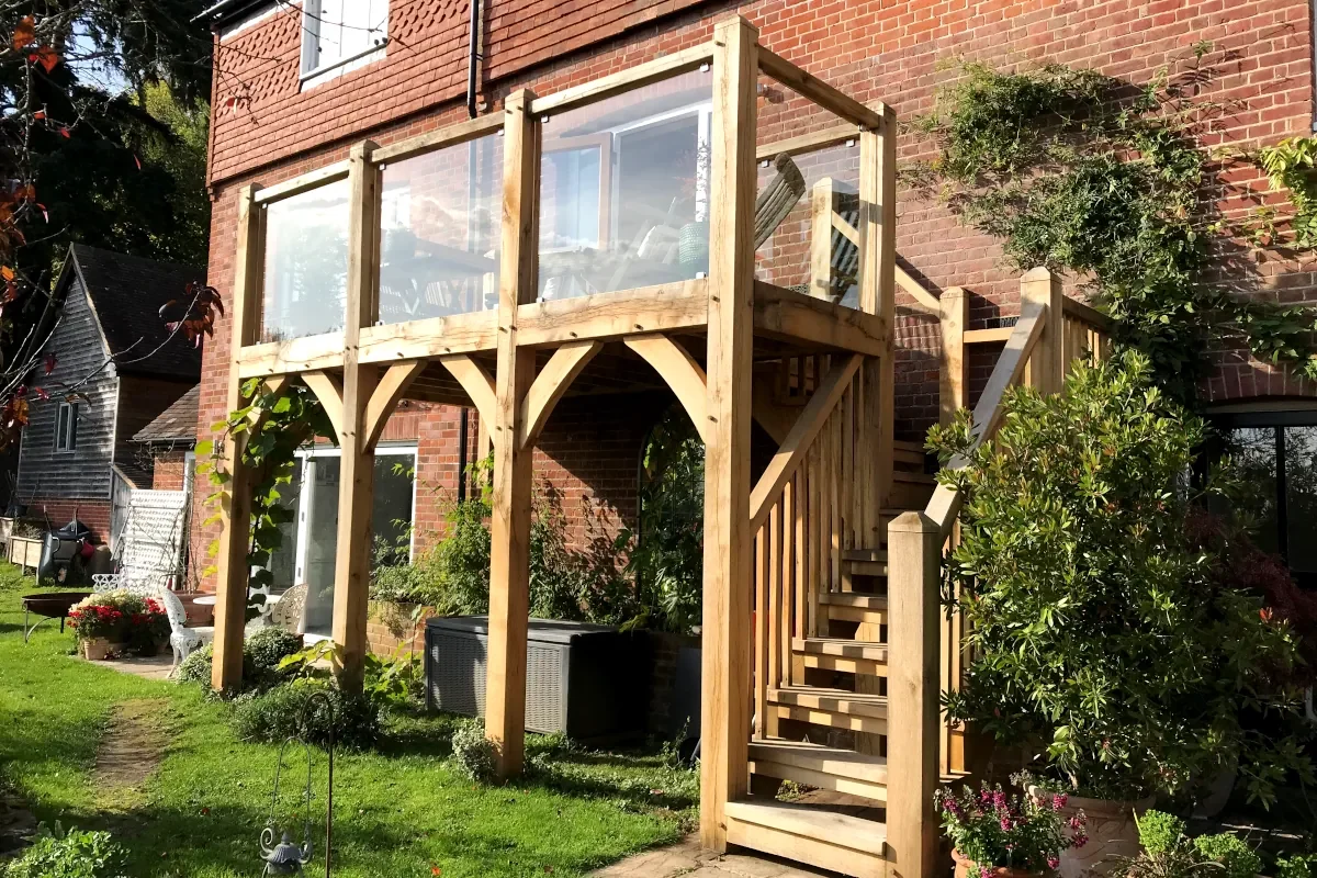 Oak Framed Balconies Bespoke oak framed balcony with glass panels and timber staircase built for a traditional brick home in rural Hampshire featuring curved braces and natural wood finish